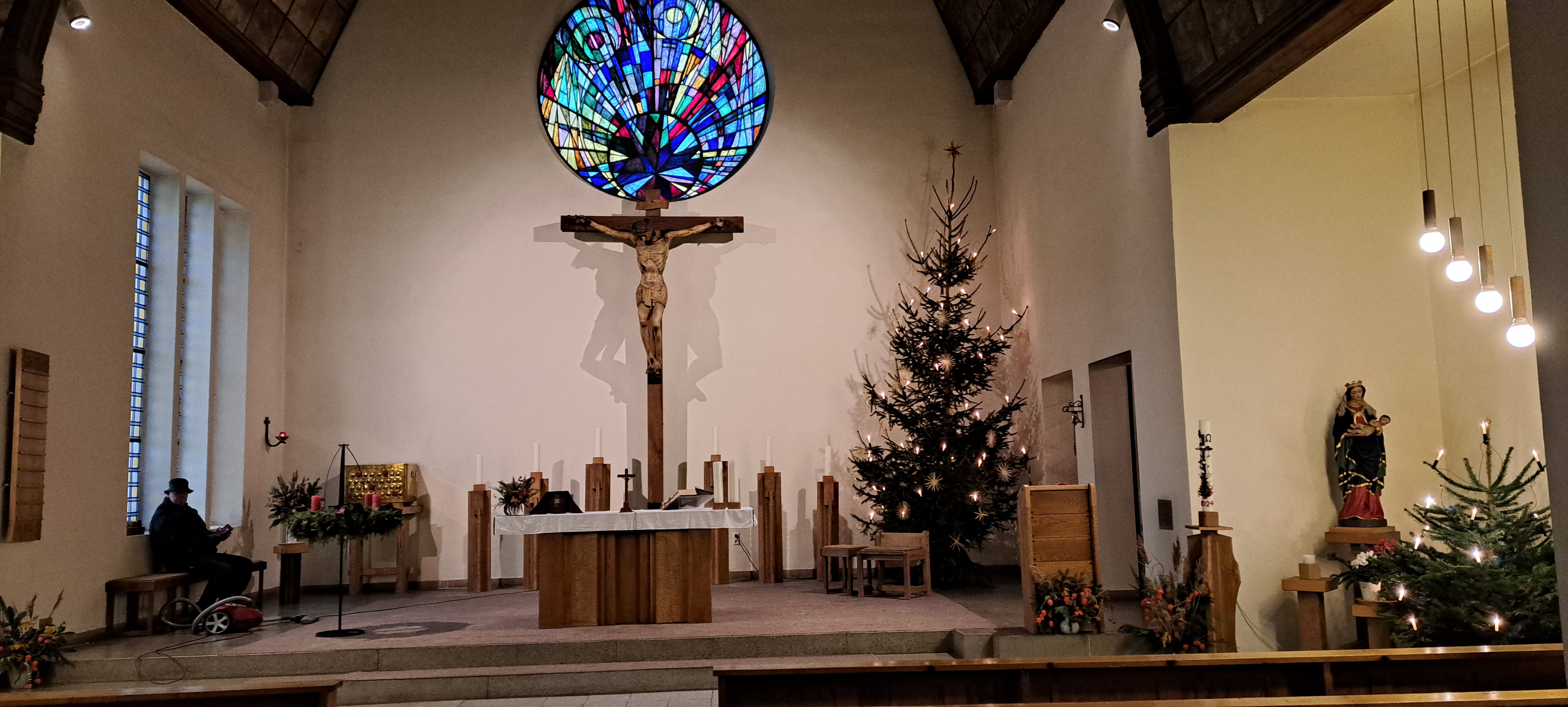 Altarraum einer Kirche mit großem Kreuz und rundem Buntglasfenster