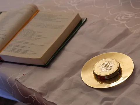 Ein goldenes Gefäß für den Leib Christi liegt zusammen mit einem aufgeschlagenen Buch auf einem weißen Altartuch