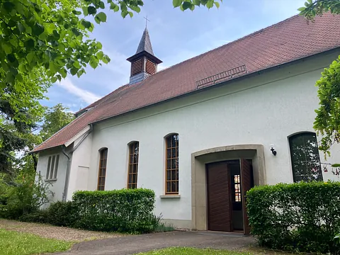 weiß gestrichenes Kirchengebäude mit roten Dachziegeln und kleinem Turm, die Tür steht offen