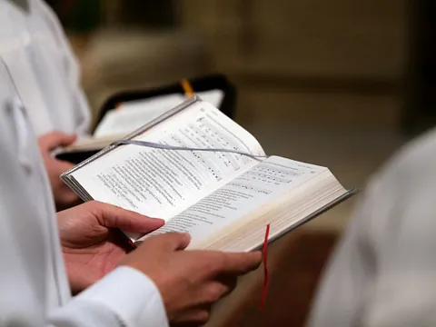 Personen in weißen Gottesdienstgewändern, die Gesangbücher halten