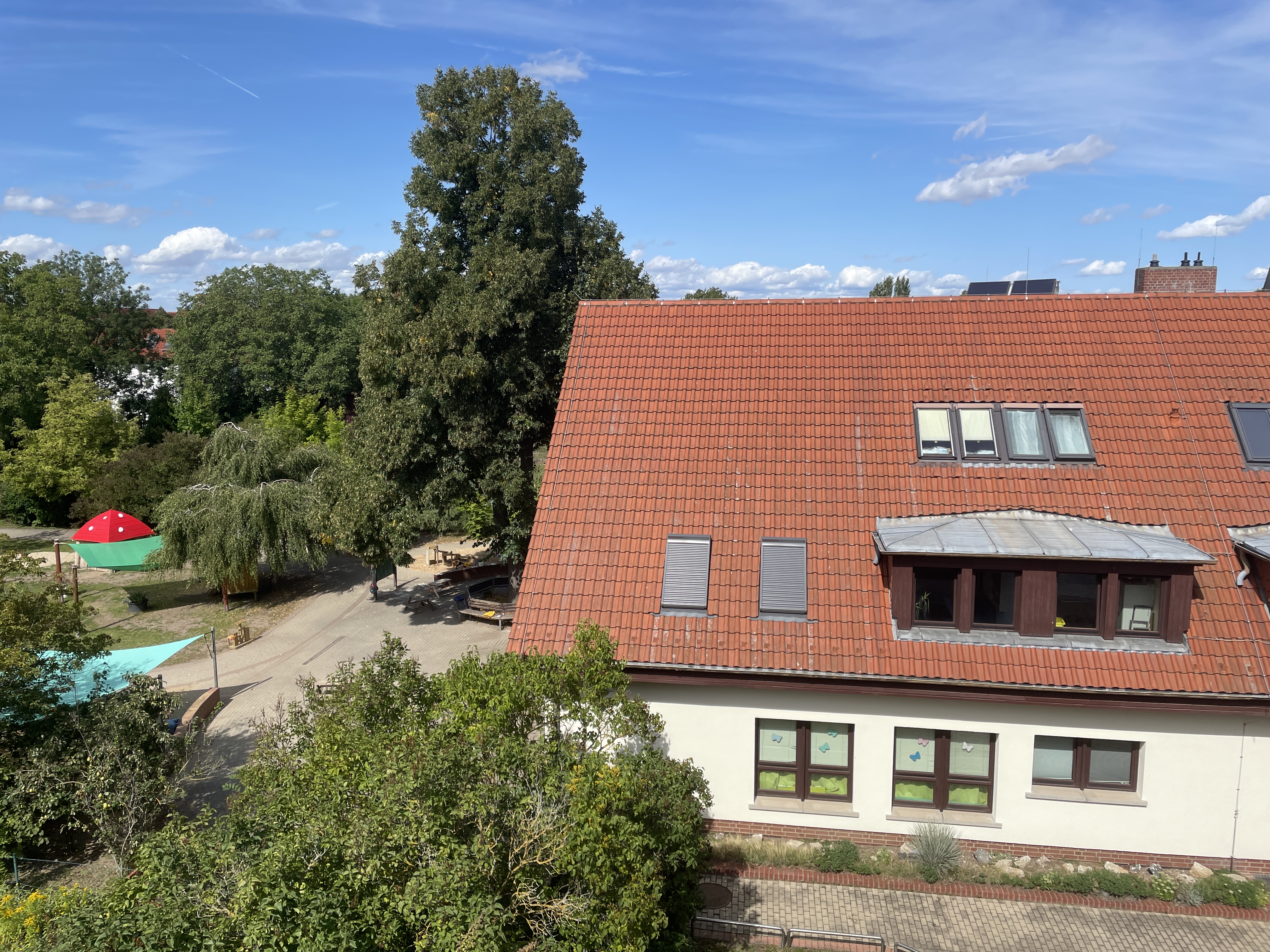 Blick von oben auf ein Gebäude mit roten Dachziegeln neben einem Spielplatz