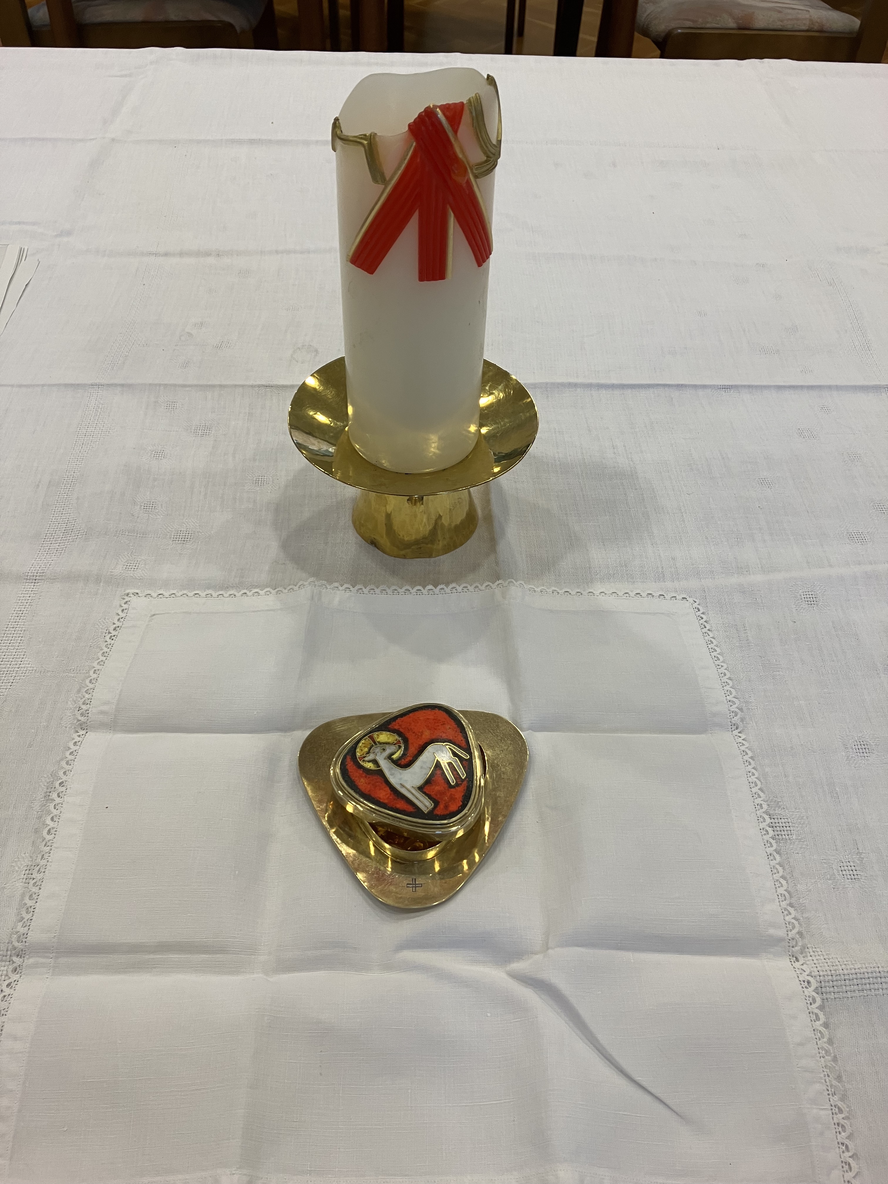 weiße Tischdecke, darauf eine Kerze und ein Gefäß für den Leib Christi, auf dem Deckel die Darstellung eines Lammes